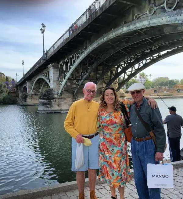 María con dos viajeros a orillas del Guadalquivir bajo el puente de Triana