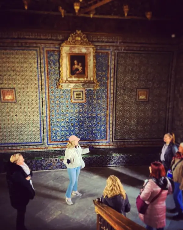 María explicando a un grupo en una sala de azulejos de un palacio sevillano